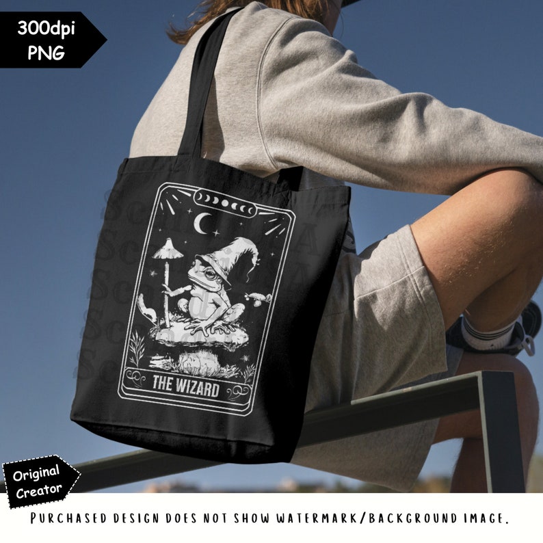 May include: A black tote bag featuring a white design of a frog wearing a wizard's hat and holding a staff. The design is in the style of a tarot card and includes the text "THE WIZARD".