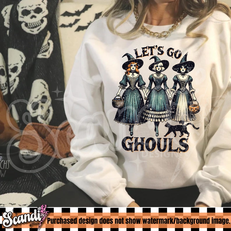 May include: White sweatshirt with a graphic of three witches in teal dresses and black hats, holding baskets and a pumpkin. The text "LET'S GO GHOULS" is printed below the witches, with a black cat. Halloween themed apparel.