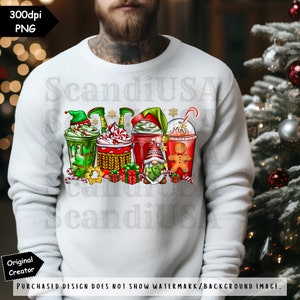 May include: A white sweatshirt with a Christmas-themed design featuring four festive drinks with gnomes, elves, and gingerbread men. The design includes red, green, and white colors.