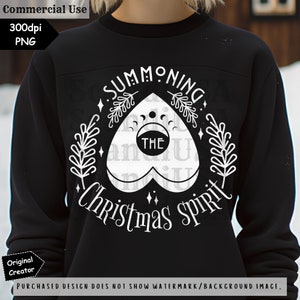 Op de afbeelding: Zwart sweatshirt met een wit grafisch ontwerp van een hartvormig Ouija-bord met de tekst "Summoning the Christmas Spirit".
