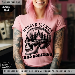 Op de afbeelding: Een roze T-shirt met een zwarte schedelprint. De hersenen van de schedel zijn vervangen door een kampvuursc&egrave;ne met bomen en sterren. De tekst "HORROR STORIES AND BONFIRES" is onder de schedel gedrukt.