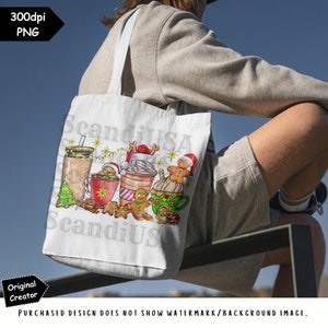 May include: A white tote bag with a Christmas-themed design featuring a gingerbread man, a mug of hot chocolate, and a cup of coffee. The design also includes a Christmas tree, a Santa hat, and a string of lights. The text "ScandiUSA" and "ScandiUS" is visible on the bag.