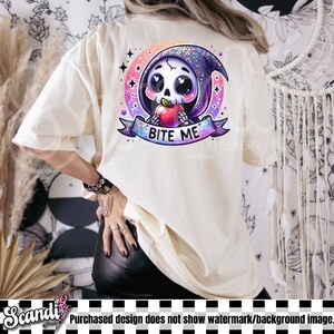 以下が含まれることがあります： クリーム色のTシャツ。フードをかぶりリンゴを持った漫画のガイコツのカラフルなグラフィック。 グラフィックは星の付いたピンクと紫の円で囲まれ、「BITE ME」の文字がバナーに書かれています。