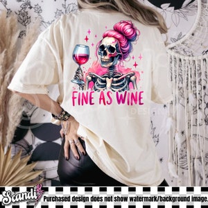 K&ouml;nnte beinhalten: Ein wei&szlig;es T-Shirt mit einem rosafarbenen Skelett, das ein Glas Rotwein h&auml;lt. Das Skelett hat rosafarbenes Haar in einem Dutt und der Text "FINE AS WINE" ist unter dem Bild gedruckt.