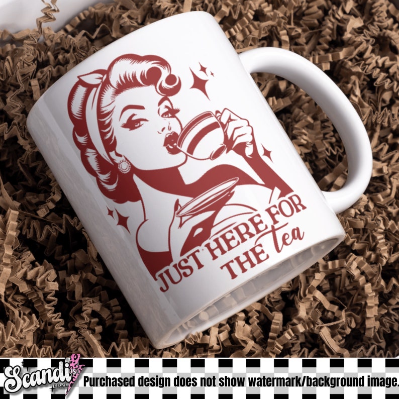 May include: White ceramic mug with a red graphic of a woman drinking tea, with the text "JUST HERE FOR THE TEA". The mug has a curved handle and is set against a brown background.