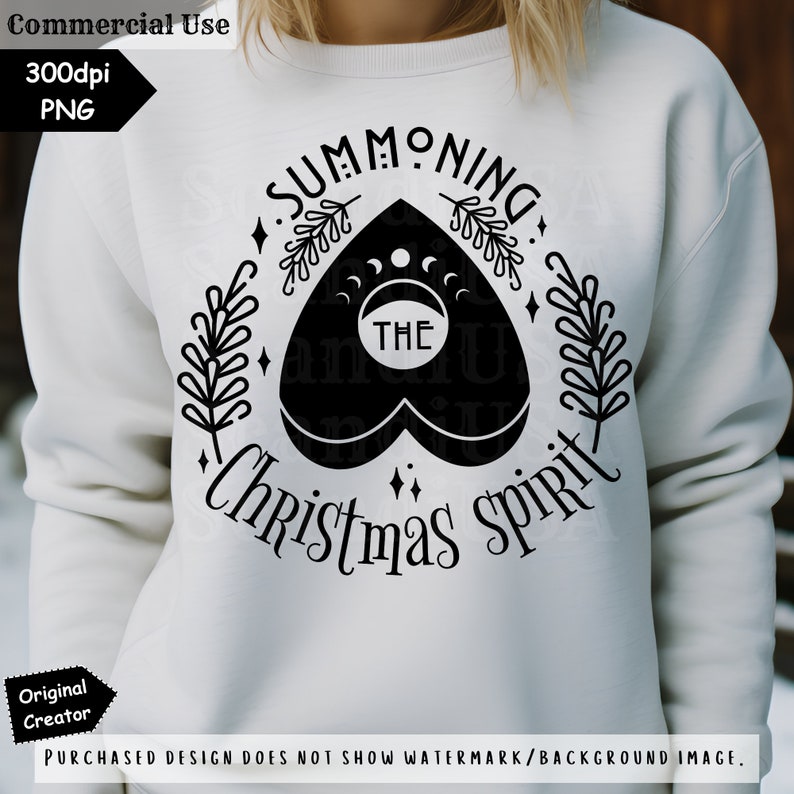 Op de afbeelding: Een wit sweatshirt met een zwart grafisch ontwerp met de tekst "Summoning The Christmas Spirit". Het ontwerp bevat een zwart hart met een wassende maan en het woord "THE" erin.