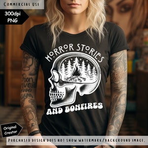 Op de afbeelding: Zwart T-shirt met een witte afbeelding van een schedel met een bos sc&egrave;ne erin. De tekst "HORROR STORIES AND BONFIRES" staat rond de schedel.