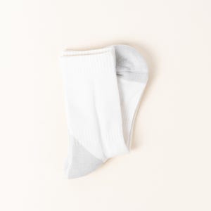 May include: A single white athletic sock with a gray heel and toe. The sock is folded over, showing the ribbed cuff and the breathable knit fabric. The sock is designed for comfort and performance.