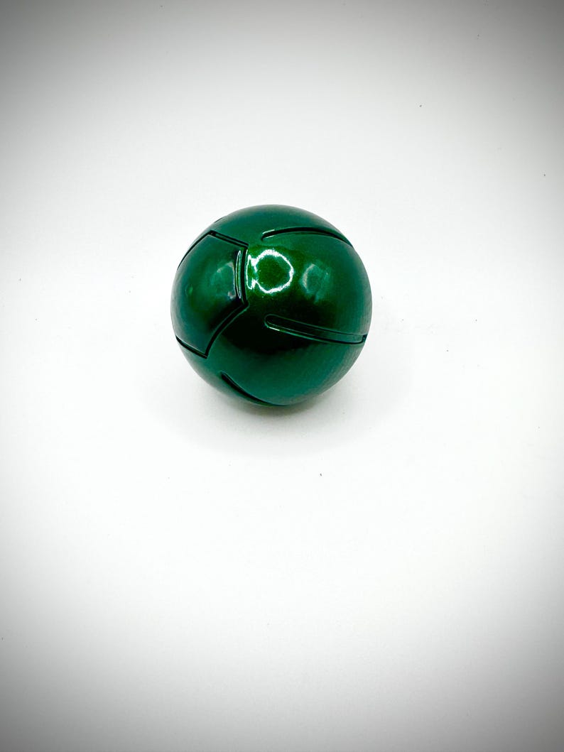 Puede incluir: Una esfera verde met&aacute;lico brillante con paneles segmentados, sobre un fondo blanco. La superficie brillante del objeto esf&eacute;rico refleja la luz, resaltando sus paneles geom&eacute;tricos. Podr&iacute;a ser un objeto decorativo o un elemento de dise&ntilde;o.