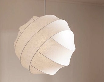 May include: A white, round, fabric pendant light fixture hangs from the ceiling above a bed with white pillows and a burgundy duvet.
