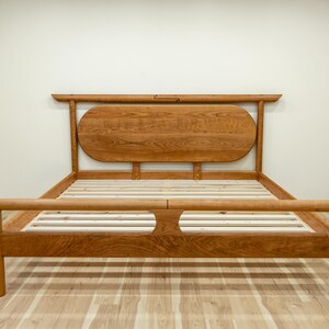 May include: A wooden bed frame with a headboard and footboard. The headboard has a rounded top and is made of light brown wood. The bed frame is made of the same wood and has a slatted base for a mattress.