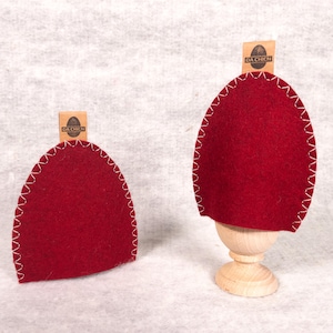 Könnte beinhalten: Zwei rote Filz-Eierwärmer mit weißen Nähten. Jeder Wärmer hat ein braunes Papieretikett mit dem aufgedruckten Text "DA CHICN".