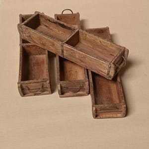 May include: A collection of six weathered wooden boxes with metal handles. The boxes are rectangular with a natural wood finish, showing signs of age and use. The handles are a dark metal color.