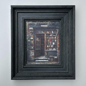 Pode incluir: Uma impressão emoldurada de uma livraria. A imagem mostra um edifício de tijolo com uma porta de madeira e prateleiras cheias de livros. A moldura é preta e tem uma aparência texturizada. A impressão é montada numa parede branca.