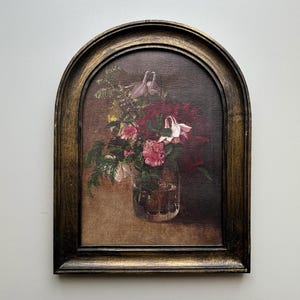 Könnte beinhalten: Ein bogenförmig gerahmtes Gemälde eines Blumenarrangements in einer durchsichtigen Glasvase. Die Blumen sind eine Mischung aus Rosa, Rot und Weiß, mit grünem Laub. Der Rahmen ist aus dunklem Holz mit goldenen Akzenten.