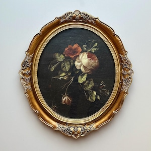 May include: An oval, gold-coloured framed painting of a floral still life. The artwork depicts roses in red and white, with green leaves against a dark background. The ornate frame adds a vintage aesthetic, suitable for home decor.