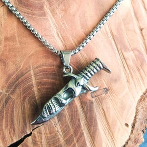May include: A silver chain necklace with a pendant shaped like a dagger with a skull design.