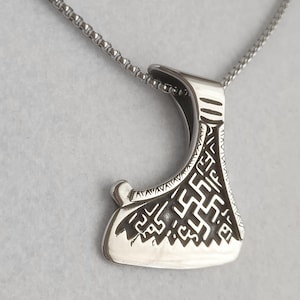 May include: A silver-colored pendant necklace featuring a detailed axe-shaped charm. The charm has intricate engraved patterns and hangs from a delicate chain. The axe head has a curved blade and a rounded handle.