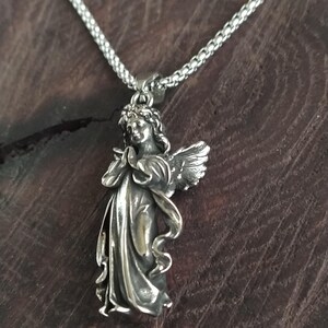May include: A silver angel pendant necklace with a detailed design. The angel is depicted with wings and a flowing robe. The necklace is made of a silver chain.