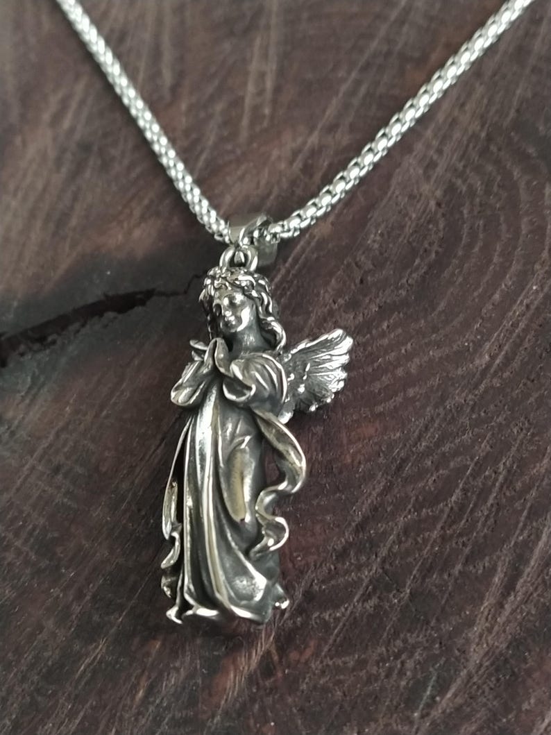 May include: A silver angel pendant necklace with a detailed design. The angel is depicted with wings and a flowing robe. The necklace is made of a silver chain.