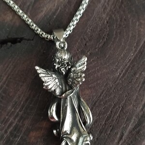 May include: A silver chain necklace with a detailed angel pendant. The angel is depicted with wings outstretched and a flowing robe.
