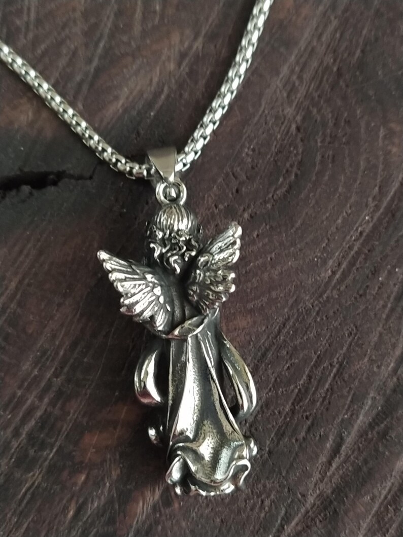 May include: A silver chain necklace with a detailed angel pendant. The angel is depicted with wings outstretched and a flowing robe.