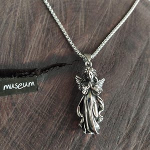 May include: A silver chain necklace with a pendant of a praying angel. The angel is detailed with wings and a flowing gown.