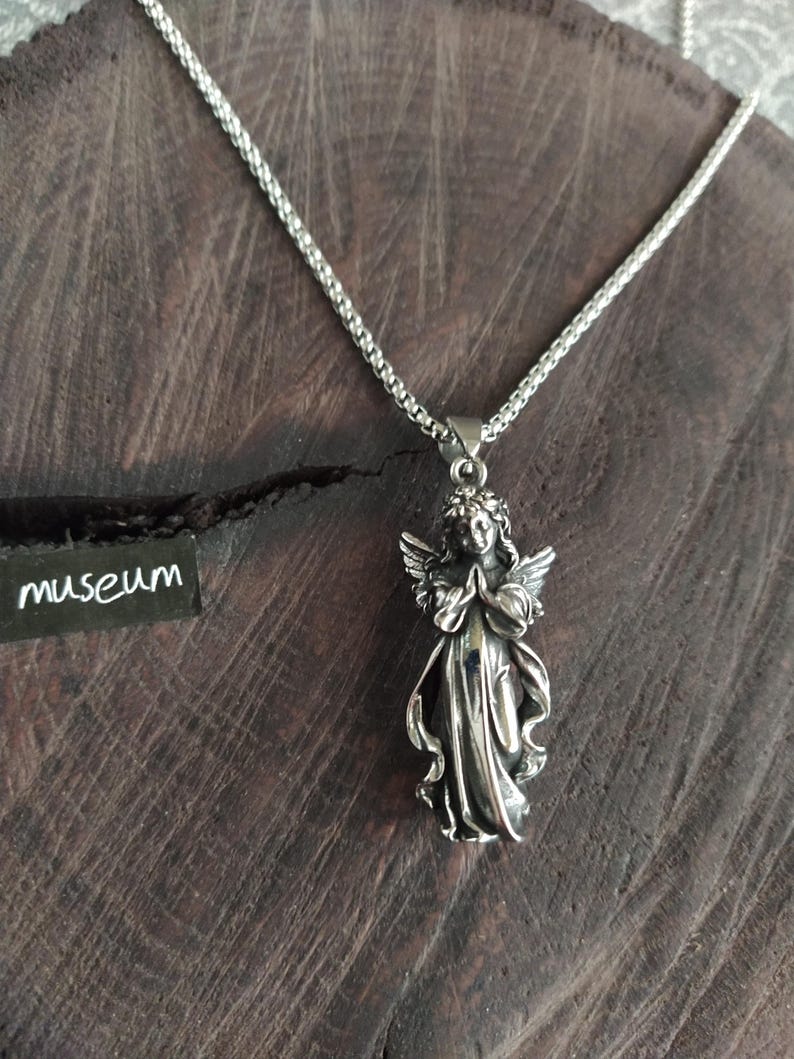 May include: A silver chain necklace with a pendant of a praying angel. The angel is detailed with wings and a flowing gown.