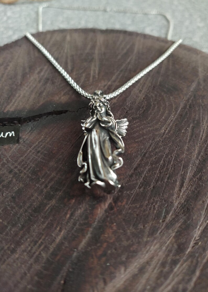 May include: A silver necklace with a detailed angel pendant. The angel is depicted with wings and a flowing gown.