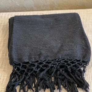 May include: A black woven blanket with a fringe border. The blanket is made of a soft, textured fabric and has a simple, elegant design.