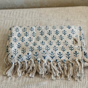 May include: A cream-coloured throw blanket with a blue geometric pattern and fringe trim. The pattern is a repeating design of small blue trees.