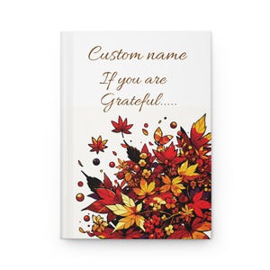 May include: A white hardcover journal featuring the brown text Custom name If you are Grateful..... and a vibrant illustration of autumn leaves in shades of red, orange, and yellow with small berries clustered at the bottom right corner.