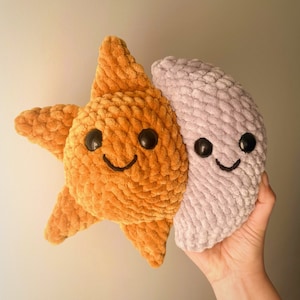 May include: A plush toy set featuring a yellow star and a purple crescent moon. Both toys have embroidered eyes and smiling mouths.