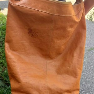 May include: A large, brown leather tote bag with a zipper closure and a shoulder strap. The bag has a logo on the front that says "The Traveler".