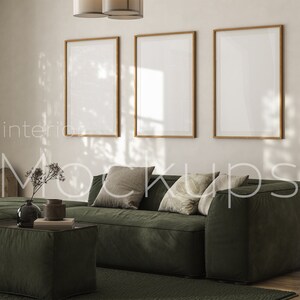 May include: Three framed posters hang on a wall above a green sectional sofa with pillows. The sofa is in a living room with a coffee table and a vase of flowers.