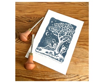 May include: A blue and white linocut print of a person reading a book under a tree with a cat and a bird. The print is titled "The Reading Tree" and is signed "Happy Birthday Sarah".