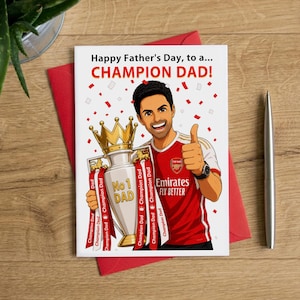 Könnte beinhalten: Eine weiße Grußkarte mit einer Cartoon-Illustration einer Person in einem rot-weißen Fußballtrikot, die einen goldenen Pokal hält. Der Text lautet Happy Father's Day, to a... CHAMPION DAD! und No 1 DAD auf dem Pokal, mit rotem Konfetti.
