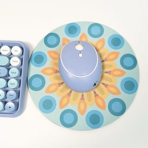 May include: A blue wireless mouse with a white button on top, sitting on a round blue and yellow patterned mousepad.