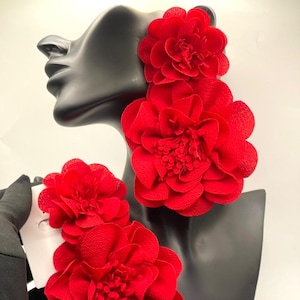 May include: Vibrant red floral earrings. The earrings, with multiple layers of petals, are displayed on a black mannequin head. The earrings are attached to white card. The earrings are a bold statement piece.