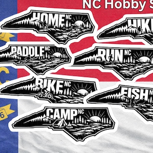May include: A collection of black and white NC Hobby Stickers featuring outdoor activities like hiking, biking, and fishing, set against the North Carolina flag. The stickers are shaped like the state.