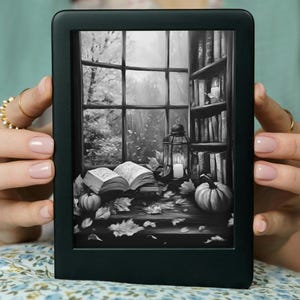 May include: A black and white illustration of a book, a lantern, and pumpkins on a table by a window. The window looks out onto a forest. The image is displayed on a black e-reader.