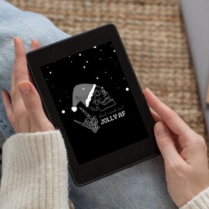 May include: A black e-reader with a white illustration of a skull wearing a Santa hat and making a rock and roll hand gesture. The text on the screen reads "dead inside but JOLLY AF".