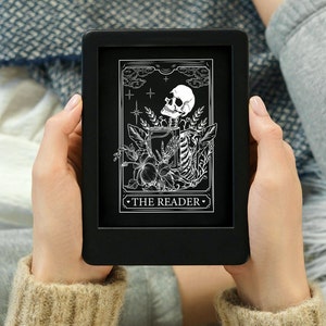 May include: A black e-reader displaying a tarot card with a white illustration of a skeleton holding a book and the text "THE READER".