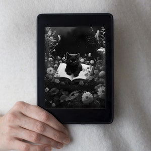 May include: A black and white image of a black cat sitting on an open book in a garden setting. The cat is looking directly at the viewer. The book is surrounded by flowers and leaves.