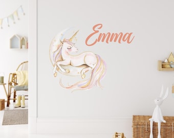 May include: A white unicorn with a gold horn and a pink mane and tail is sleeping on a crescent moon with gold stars. The unicorn is surrounded by a pink and purple glow. The name "Emma" is written in pink cursive above the unicorn.