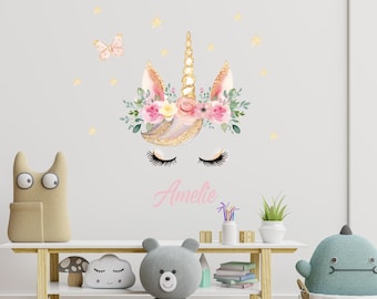 May include: A white unicorn head with a gold glitter horn and pink flowers around the horn. The unicorn has closed eyes and long eyelashes. The name "Amelie" is written in pink below the unicorn.