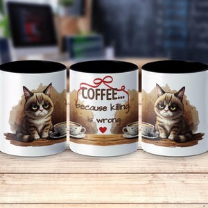 Puede incluir: Taza de café de cerámica blanca con interior y asa negros. La taza presenta una ilustración de un gato gruñón con una taza de café y el texto "Coffee... because killing is wrong."