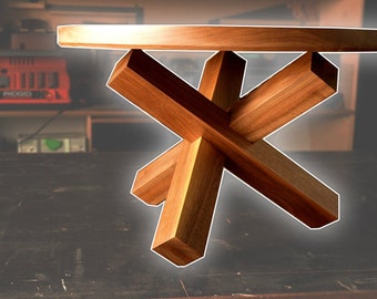 May include: A wooden table with a round top and a unique X-shaped base. The table is made of light brown wood and has a natural finish.