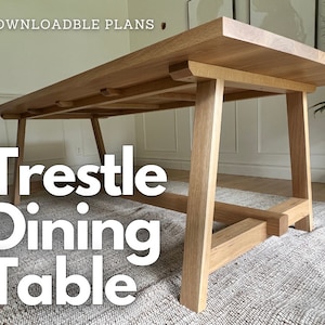 Op de afbeelding: Een houten eettafel met een trestle-onderstel en een natuurlijke houtkleur. De tafel heeft een rechthoekig blad en twee trestle-poten aan elke kant. De tafel staat op een tapijt.