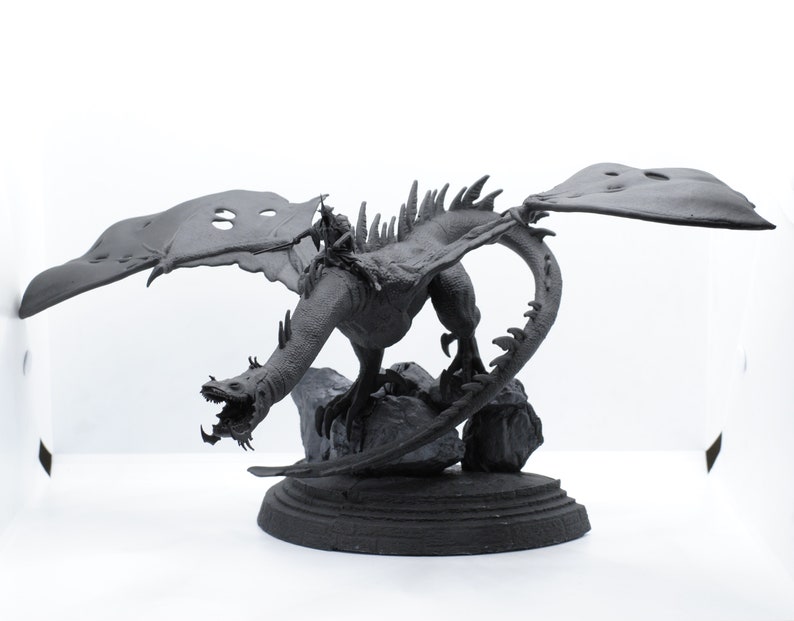 Puede incluir: Una figura de drag&oacute;n negro con las alas extendidas, posada sobre una base rocosa. El drag&oacute;n tiene una superficie detallada y texturizada y una expresi&oacute;n feroz.